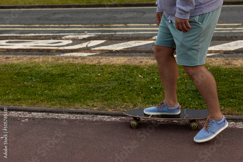 Close-up view from above men's legs in green shorts on a skateboard.