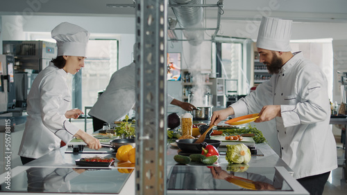 People cooking professional food recipe in restaurant kitchen, using fresh vegetables to prepare gourmet meal. Diverse team of cooks making authentic menu dish for gastronomy cuisine service. © DC Studio