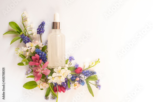 Cosmetic glass transparent bottle with dropper for hyaluronic acid among different wildflowers on a white background. Beautiful light reflections.
