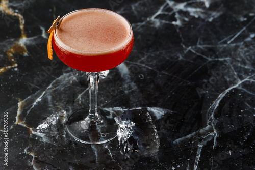 A red sour cocktail in a coupe glass garnished with an orange peel. Clover club with imported gin.