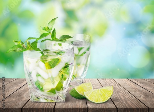Fresh lemonade drink or alcoholic cocktail with ice, mint and lemon slices on blur background.