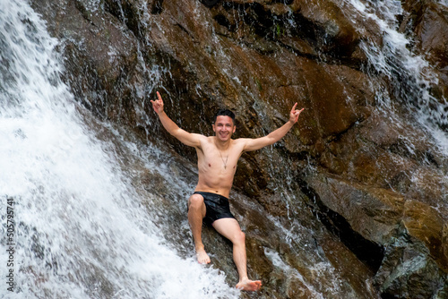 hombre joven sonriendo  sentado en una roca  en una cascada 