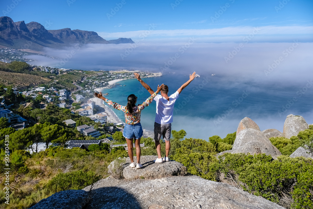 Φωτογραφία Couple men and women with hands up standing on a mountain top The Rock viewpoint in Cape Town over Campsbay, with fog over the ocean
