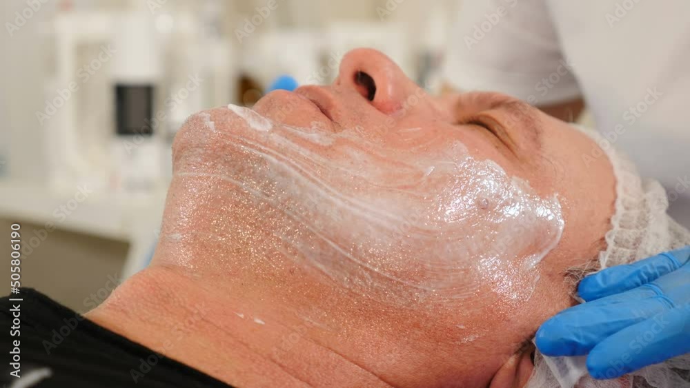 Beautician applies skrab to aged male face with hands in gloves. Skincare dermatology treatment. Mature man getting professional facial procedure. Cosmetology, cosmetic procedures for men. 4 k video Beautician applies skrab to aged male face with hands in gloves. Skincare dermatology treatment. Mature man getting professional facial procedure. Cosmetology, cosmetic procedures for men. 4 k video