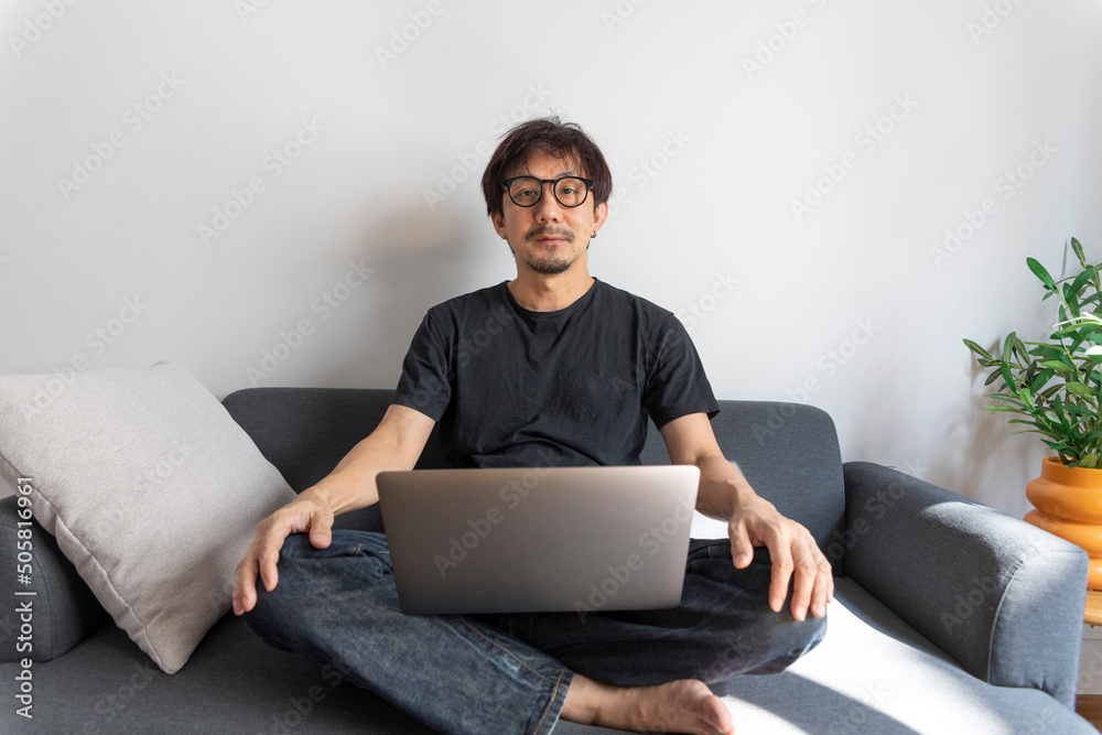 Adult handsome man making video call with friends via laptop while sitting on sofa at his modern home. Adult handsome man making video call with friends via laptop while sitting on sofa at his modern home.