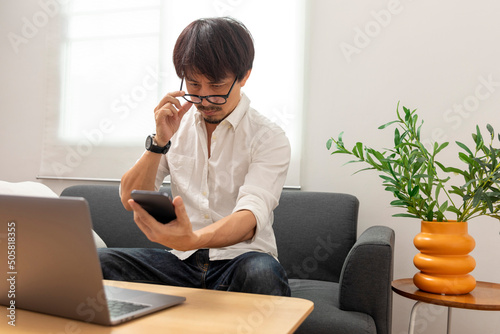 Middle age Asian man squint eye to look at the phone due to long eye sighted problems, which makes vision difficult.