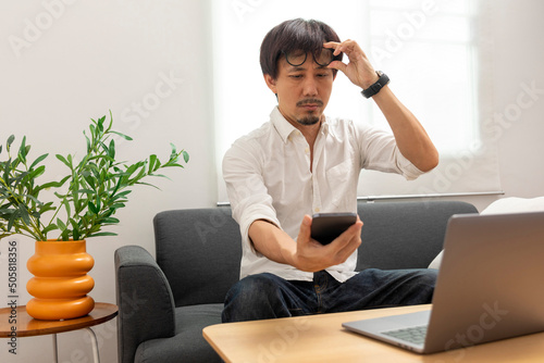Middle age Asian man squint eye to look at the phone due to long eye sighted problems, which makes vision difficult.