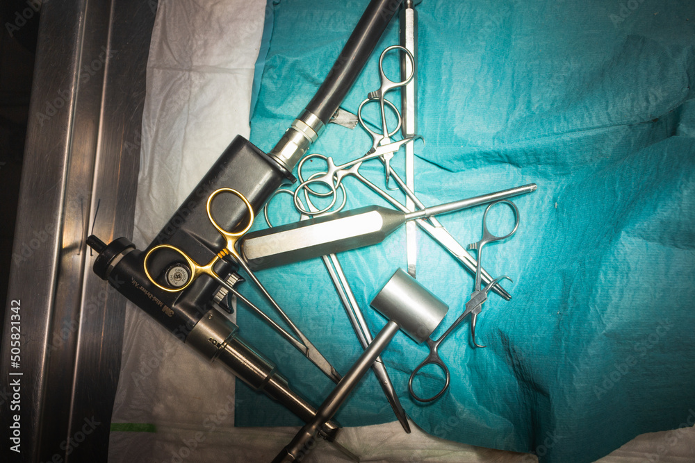 Top view of medical tools with veterinary forceps, clamps, chisel and hammer isolated on blue surgical cloth.