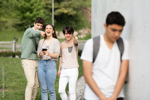 Group of teenagers laughing at hispanic boy. Racism and bullying concept.
