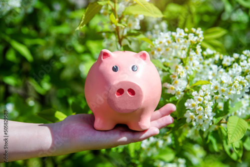 Girl holding piggy Bank against the background of blossoming Bird cherry 