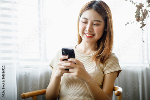 Happy millennial hispanic teen girl checking social media holding smartphone at home. Smiling young asian woman using mobile phone app playing game, shopping online, ordering delivery relax on desk.