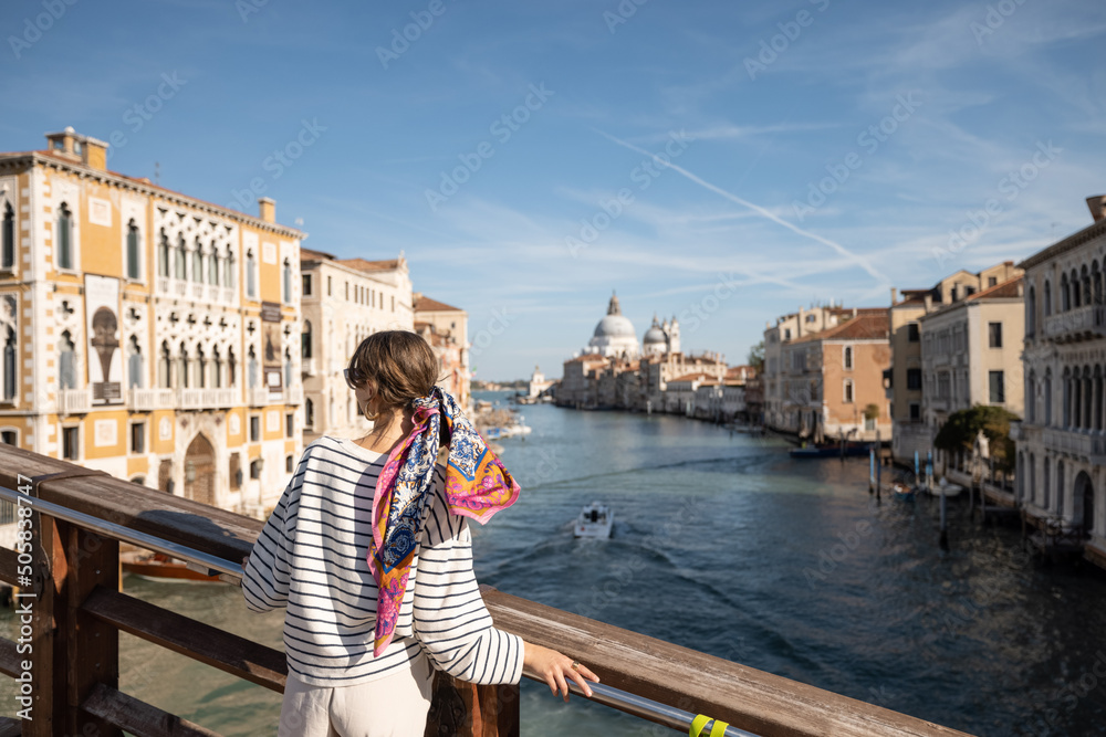 Young woman enjoying beautiful view on Grand Canal from Academy bridge in Venice. Idea of spending summer time and travel in Italy. Caucasian female wearing striped vest and colorful shawl