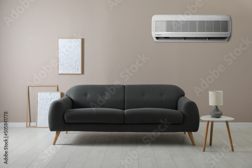 Modern air conditioner on beige wall in living room with stylish sofa