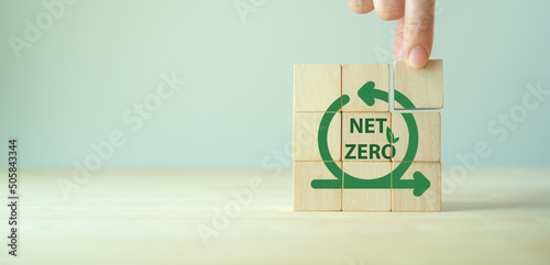 Net zero, zero emissions. Carbon neutral. Greenhouse gas emissions target. Climate neutral long term strategy. Sustainability. Holding wooden cubes with net zero emissions icon on grey background.