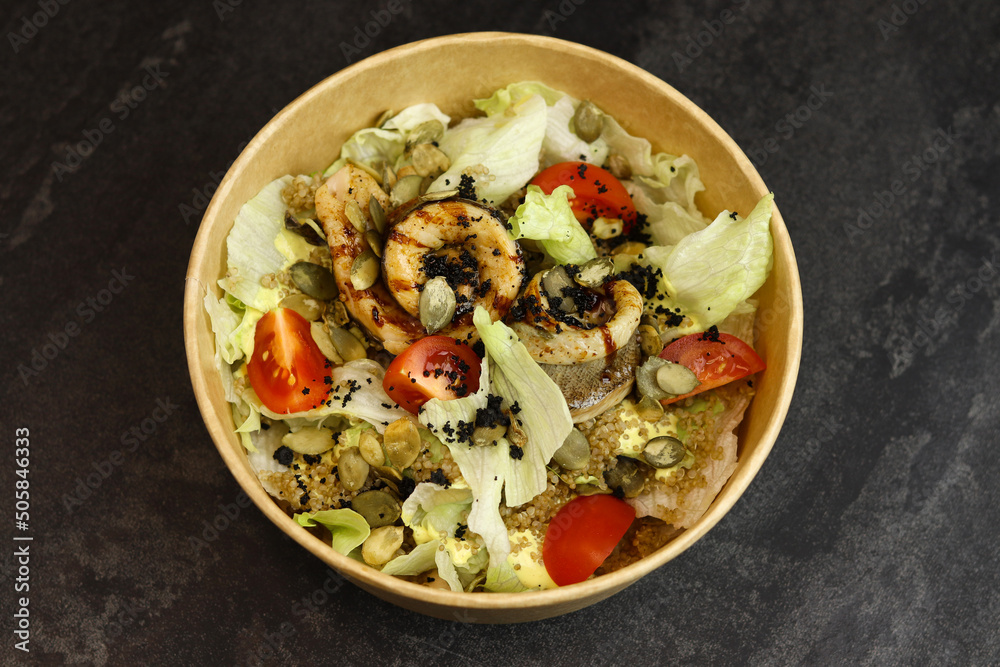 Salad with fish. Fresh vegetable salad with baked fish fillet. Fish salad with fried fillet and fresh vegetables in eco paper bowl on dark background. Food delivery service and daily ration concept.