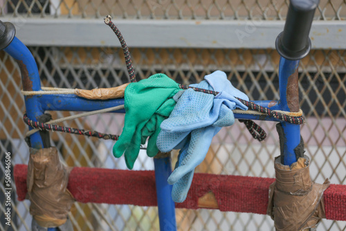 Photos Close up of vintage blue bicycle handlebars wrapped with makeshift protective gear, old cloth, and green and light blue work gloves on a rustic background