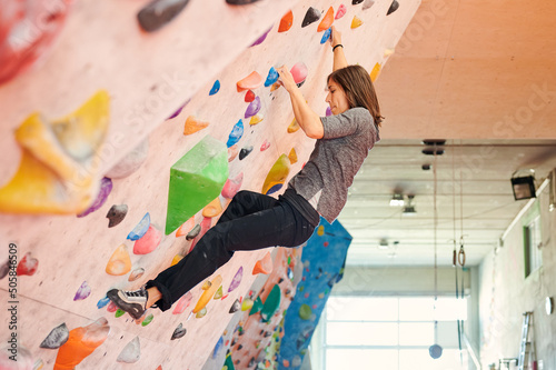Side view of focused female climber ascending angled wall during boulder workout in sunlit gym