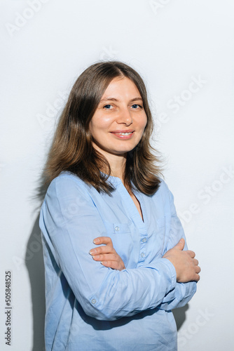 Woman sincerely smiles and stands on a white background in a blue shirt with flowing hair. Mother's Day.