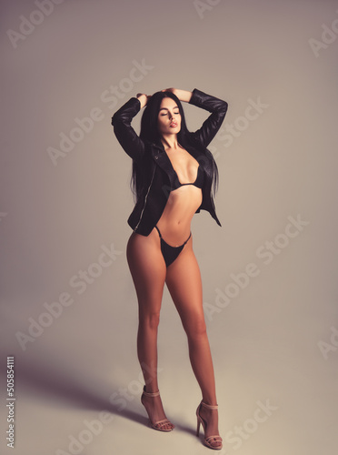 Beautiful sexy adult brunette woman in a leather jacket worn on her naked body. Grey background. Vertical.