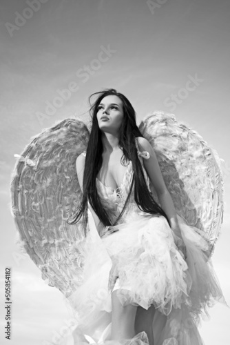 Sweety angel, woman with wings. Sensual female angel posing over a cloudy sky with feathers.
