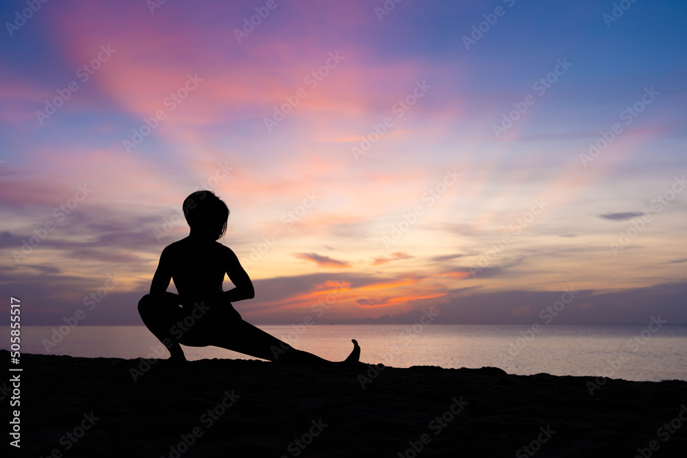 Silhouette of beautiful woman practicing yoga asana on the beach with sunrise on twilight blue vibrant sky and calm sea in background. Skandasana, Side lunge, Stretching, Power concept, Meditation.