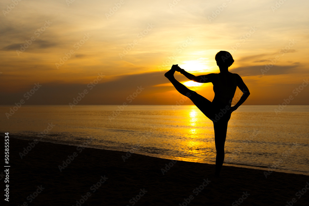 Silhouette of beautiful woman standing one leg in yoga pose on the beach with sunrise in background, Stretching, Balancing. Yoga poster, Backdrop, Wellness, Wellbeing concept, Yoga day, Copy space.