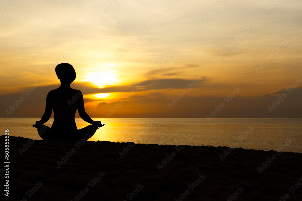 Silhouette of beautiful woman sitting cross legged in easy seat pose on the beach with sunrise in background, relaxing deep breathing meditating body and mind. Yoga poster, Backdrop, Balancing concept