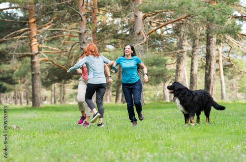 three mature women having fun playing together in the forest, celebrating reunion in nature together with their dog