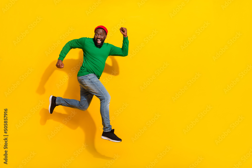 Photo of sportive cheerful crazy guy jump run have fun wear red beanie green shirt isolated yellow color background