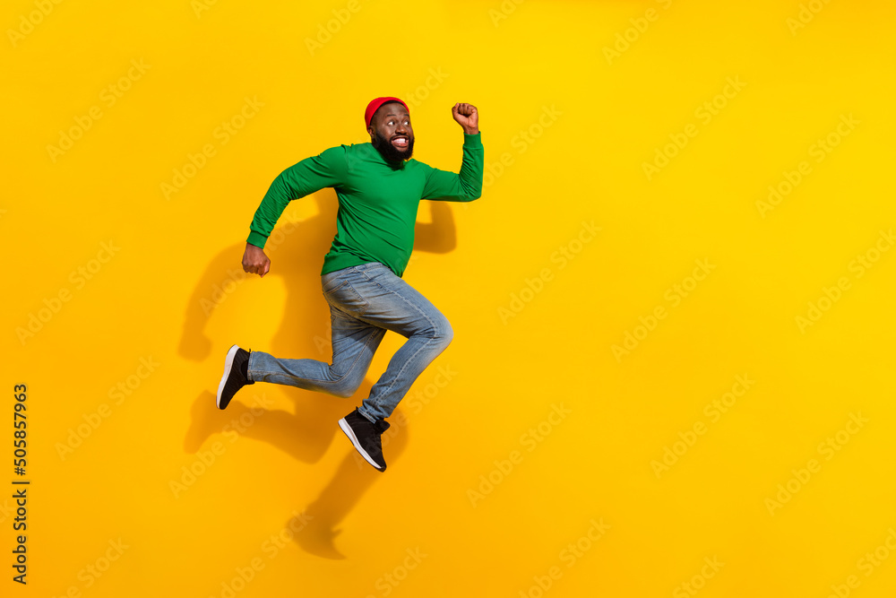 Photo of sporty energetic active guy jump rush side empty space wear red beanie green shirt isolated yellow color background