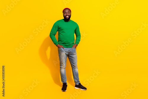 Photo of cheerful positive confident man hands pockets wear red beanie green shirt isolated yellow color background