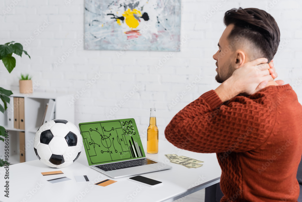 Φωτογραφία upset bookmaker touching neck near credit cards and laptop with sports game strategy on screen