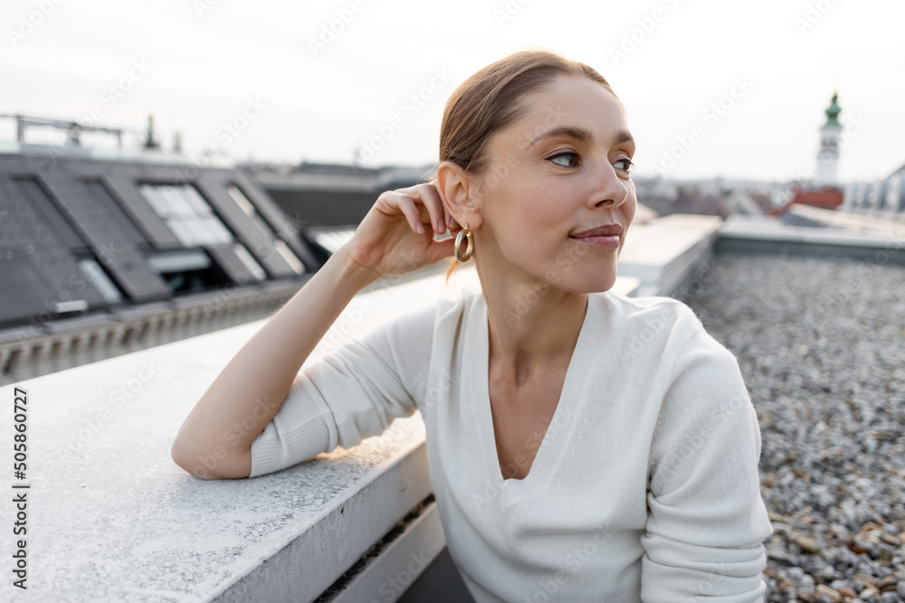 smiling woman in white jumper looking away on rooftop of city building