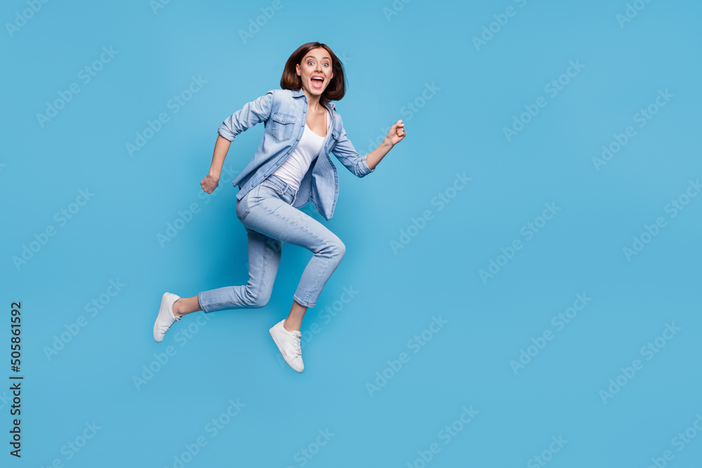 Photo of pretty excited woman wear jeans shirt hurrying jumping high isolated blue color background