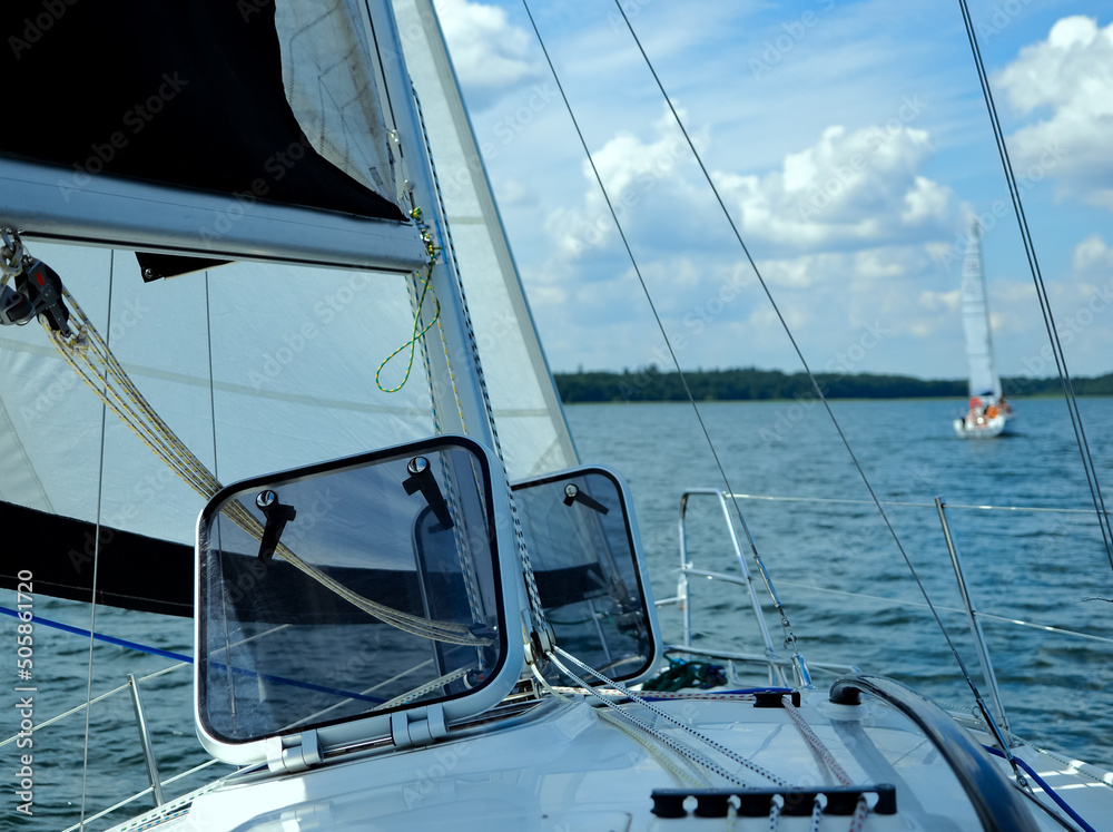 View from the yacht deck to the bow and sails, open forehatches on a sail boat. Summer voyage and sailing on a lake