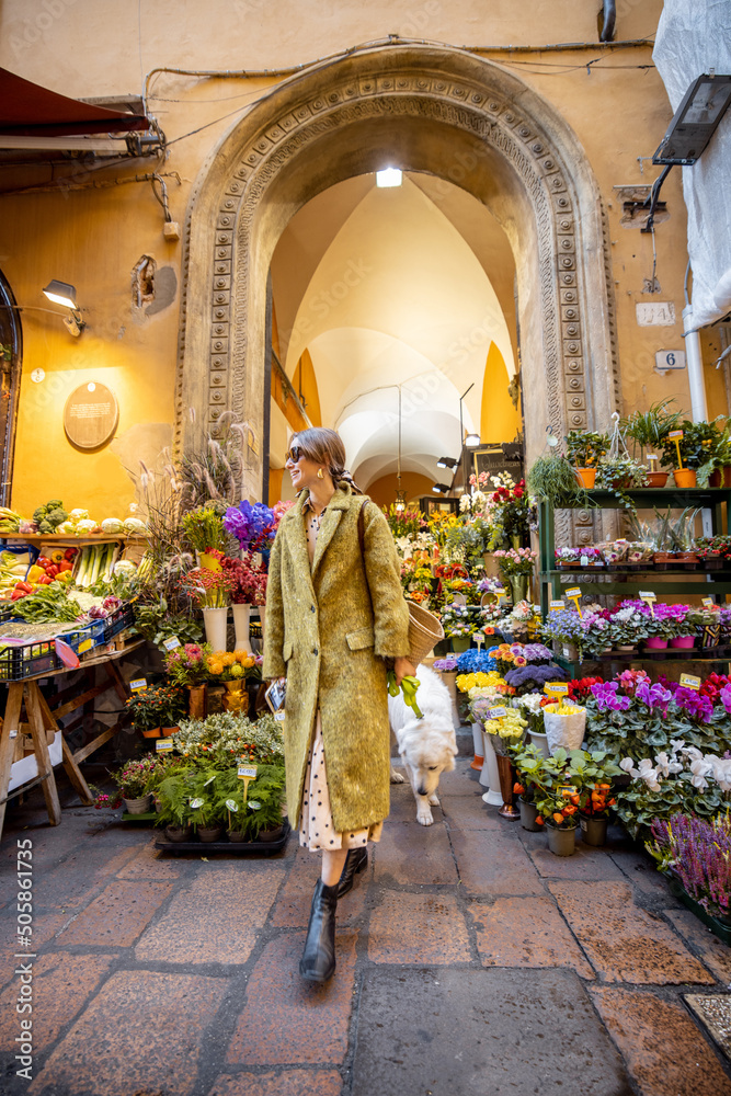 Street view on beautiful florist shop with lots of flowers in the old town of Bologna city. Italian woman walking with her dog