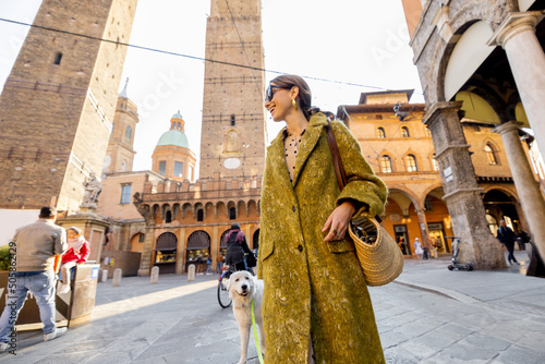 Stylish woman walks the street on background of famous towers in Bologna city. Italian lifestyle and street fashion concept. Idea of traveling Italy