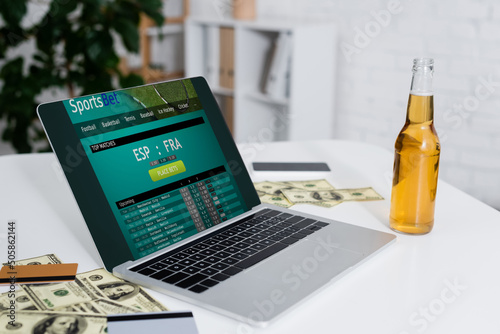 KYIV, UKRAINE - FEBRUARY 4, 2022: credit cards, dollar banknotes and beer near laptop with sportsbet website. photo