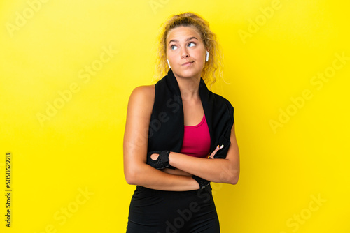 Sport woman with towel isolated on yellow background making doubts gesture while lifting the shoulders