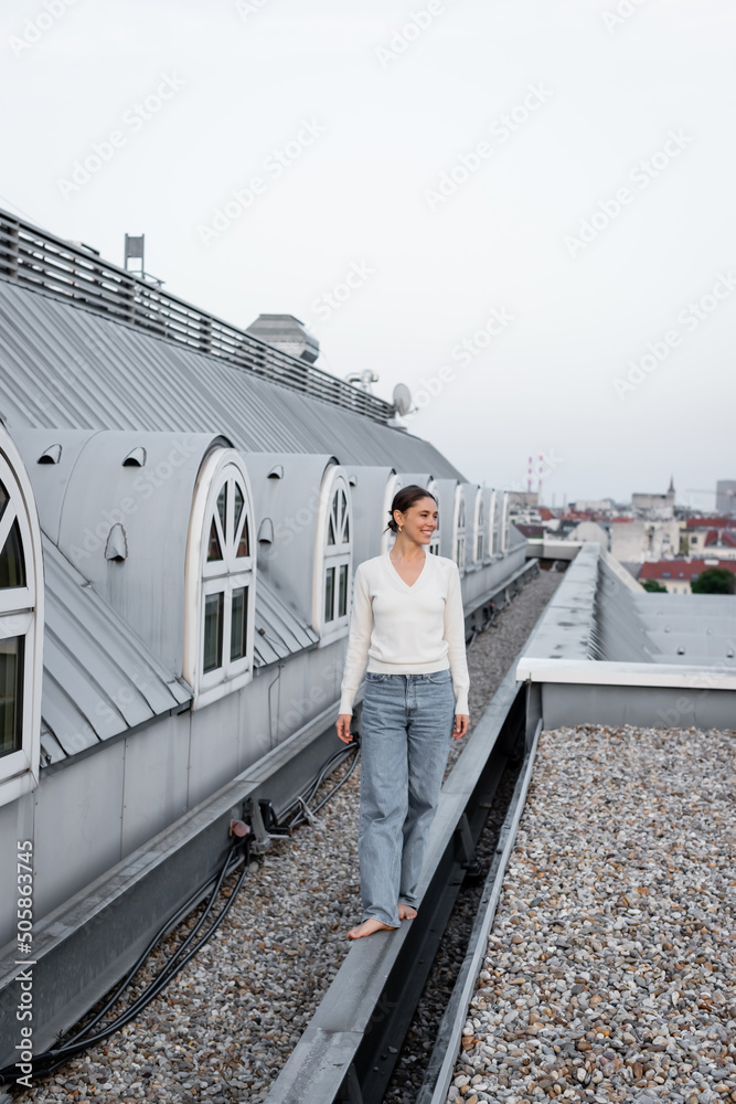 full length of barefoot woman in jeans walking on rooftop of urban ...