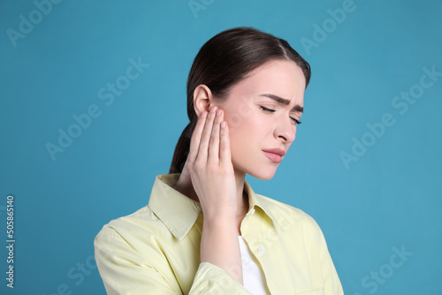Young woman suffering from ear pain on light blue background photo