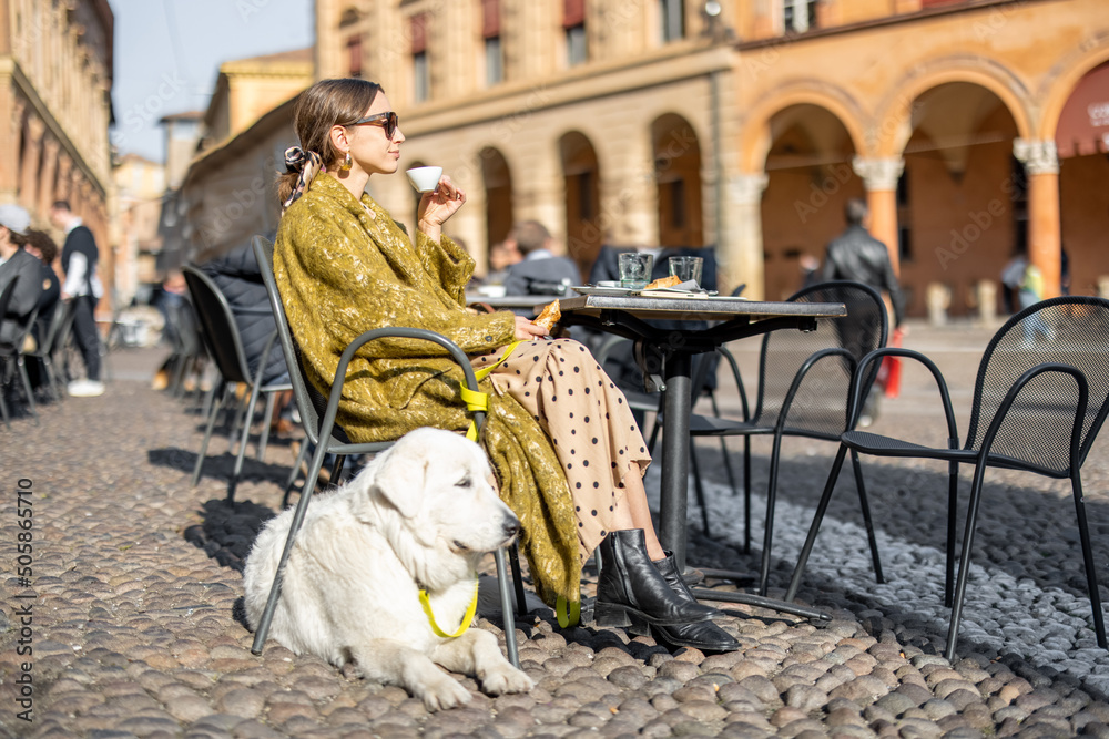 Φωτογραφία Stylish woman sitting with her white dog at outdoor cafe in the old town of Bologna city