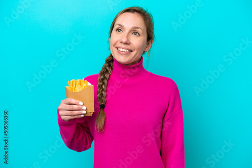Young caucasian woman holding fried chips isolated on blue background thinking an idea while looking up