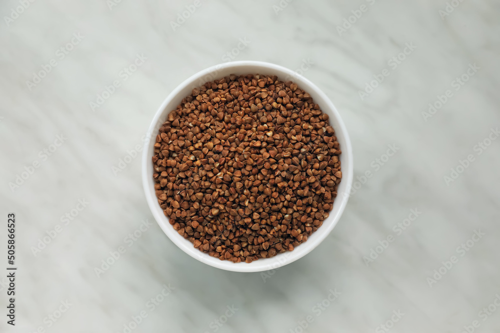 Bowl with uncooked buckwheat porridge on white marble table, top view Bowl with uncooked buckwheat porridge on white marble table, top view
