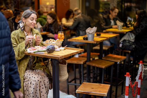 Fototapeta Naklejka Na Ścianę i Meble -  Woman eating italian meat appetizer, various sliced meat and cheese with bread and Aperol Spritz at bar or restaurant outdoors. Concept of Italian lifestyle and gastronomy