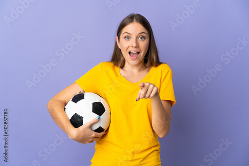 Young Lithuanian football player woman isolated on purple background surprised and pointing front © luismolinero