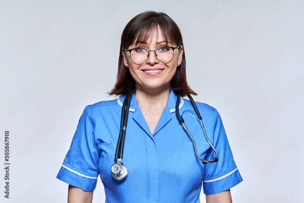 Headshot portrait of nurse in blue uniform looking at camera on light studio background Headshot portrait of nurse in blue uniform looking at camera on light studio background