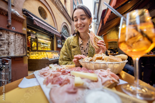 Woman eating italian meat appetizer, various sliced meat and cheese with bread and Aperol Spritz at bar or restaurant outdoors. Concept of Italian lifestyle and gastronomy