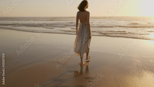 Slow motion woman walking barefoot by beach at golden sunset