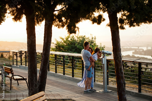 Traditional full family of father, mother and child. Happy couple of parents with a child looking at the sunset on the sea or ocean horizon through binoculars on the observation deck. Bulgaria, Varna
